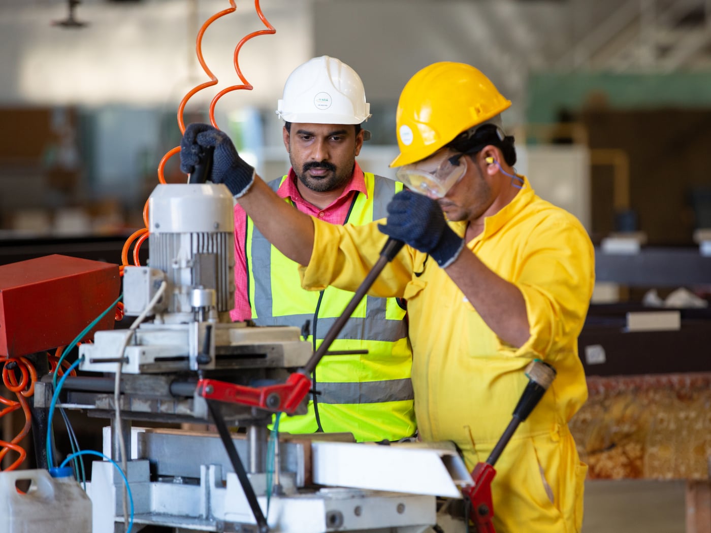 A supervisor in a white helmet working the machine alongside the man operating it