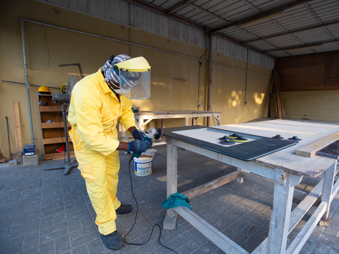 Face shield, respirator, gloves and coveralls — PPE mid-task, not on a hook